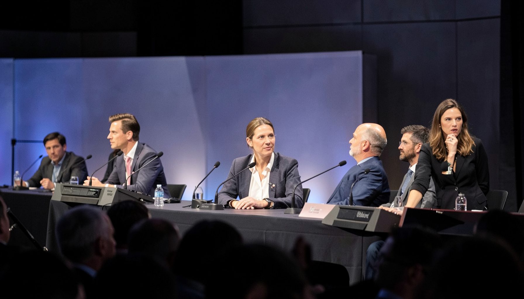 Panel of speakers at a media production industry event, softly lit stage with microphones and a moderator, professional and focused atmosphere